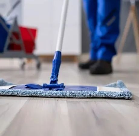 Person mopping a wooden floor with a blue mop in a room. Cleaning cart in the background.
