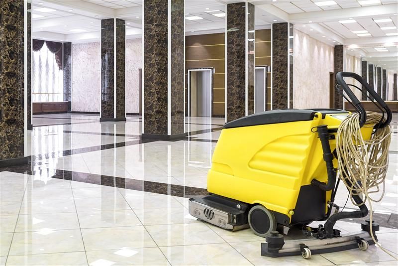 Yellow floor cleaning machine in large, shiny tile hallway.
