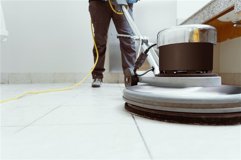 Person cleaning a tile floor with a floor buffer.