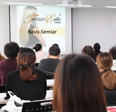 Eine Gruppe von Menschen sitzt vor einer Leinwand, auf der „Basis-Seminar“ steht