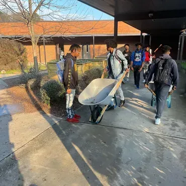 A group of young men are pushing a wheelbarrow down a sidewalk.