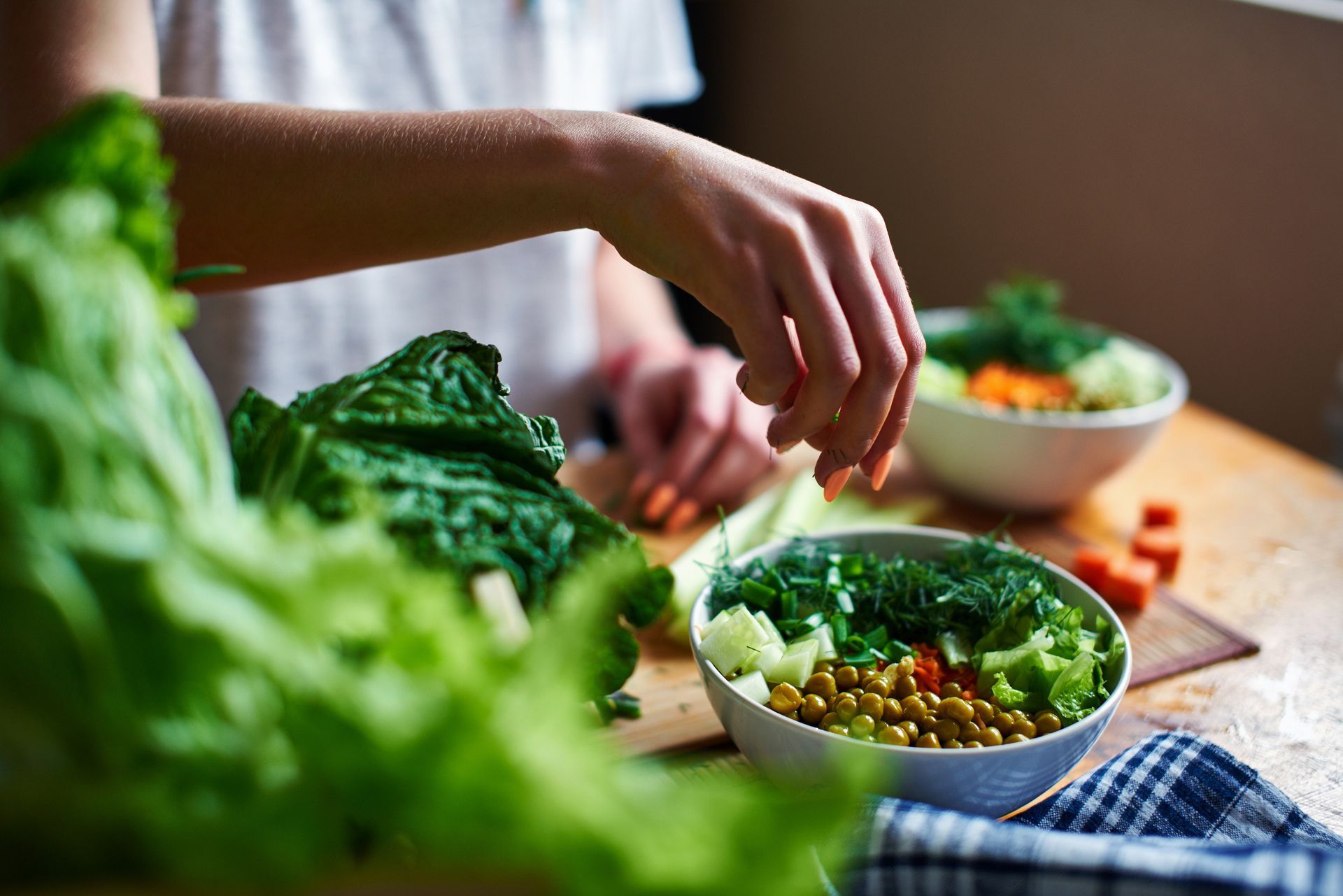 A person is preparing a salad in a bowl on a table.
