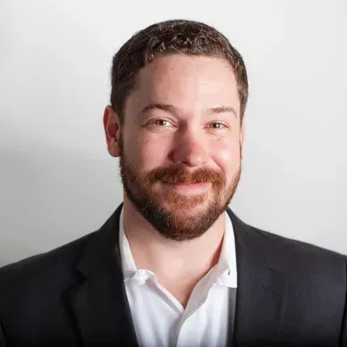 A man with a beard is wearing a suit and smiling for the camera.