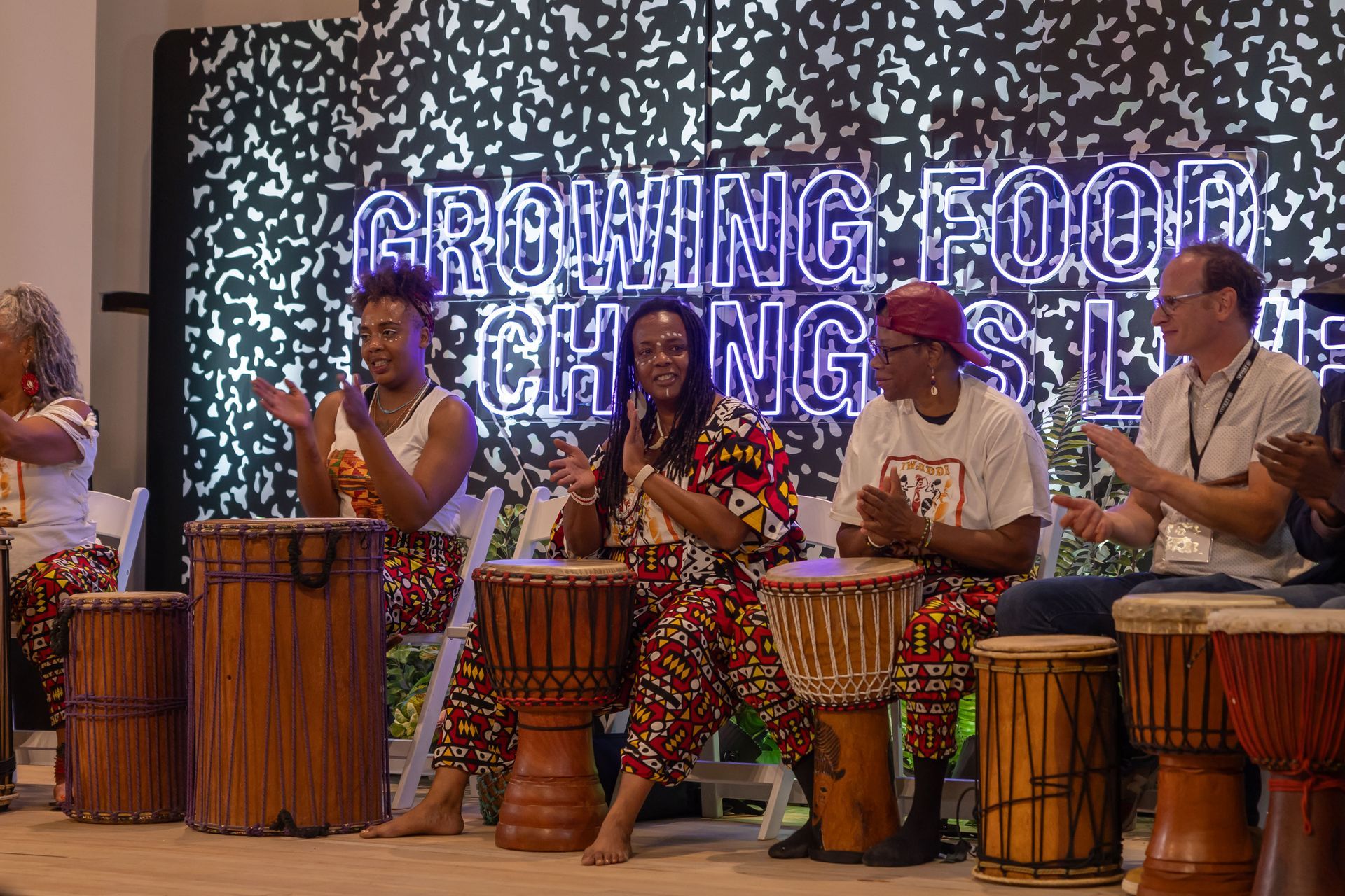 A group of people are sitting around drums on a stage.
