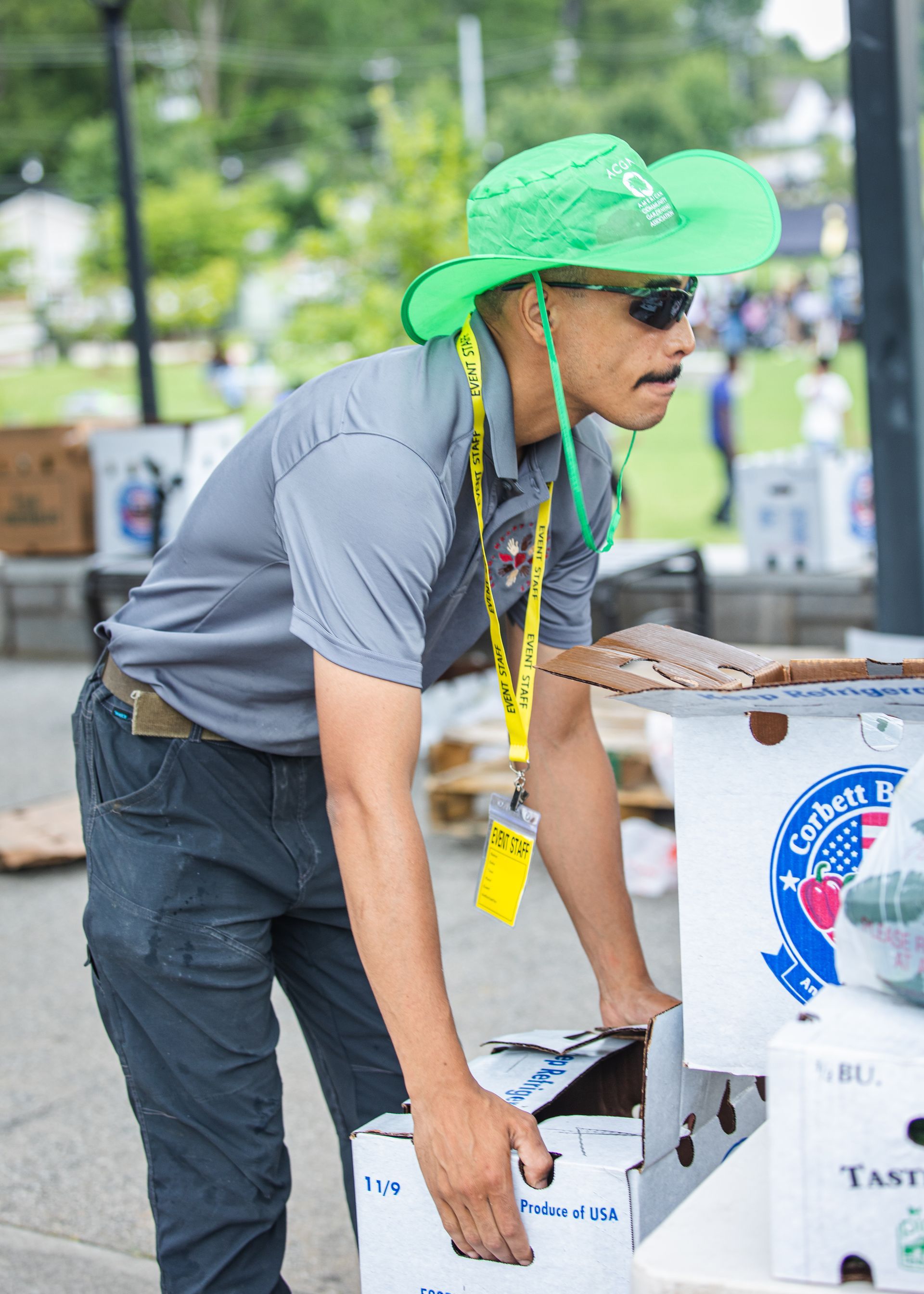 A man wearing a green hat is reaching into a box.