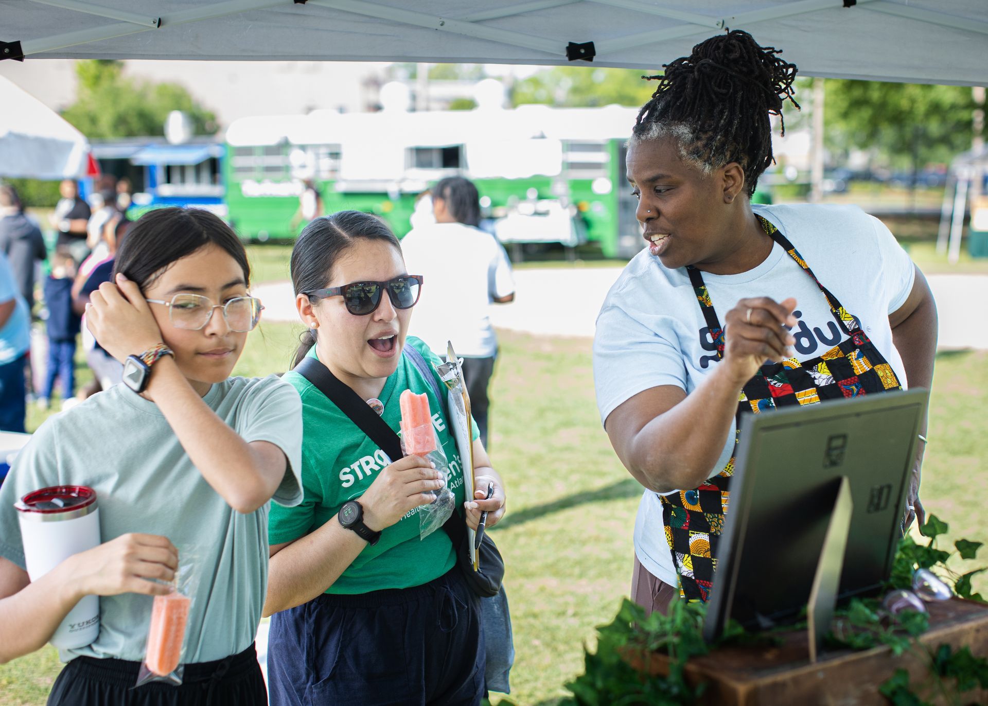 A group of people are standing under a tent eating popsicles.