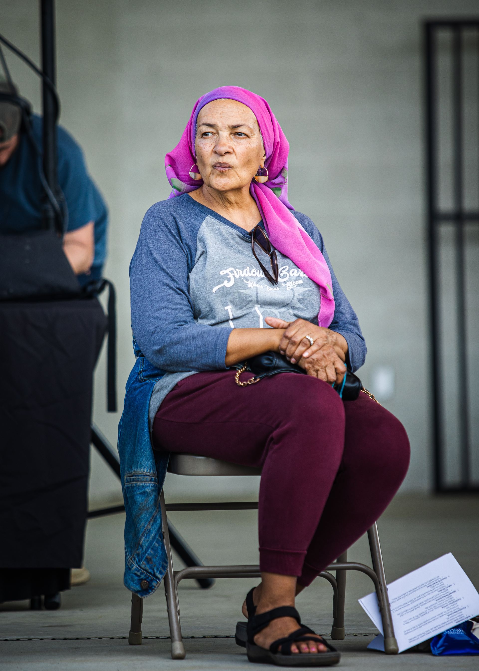 A woman wearing a pink head scarf is sitting in a chair.