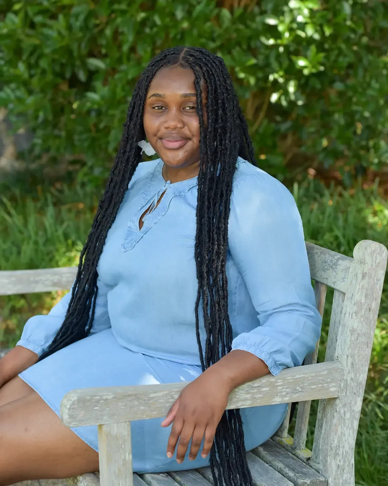A woman in a blue dress is sitting on a wooden bench.