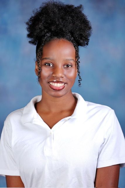 A woman in a white polo shirt is smiling for the camera