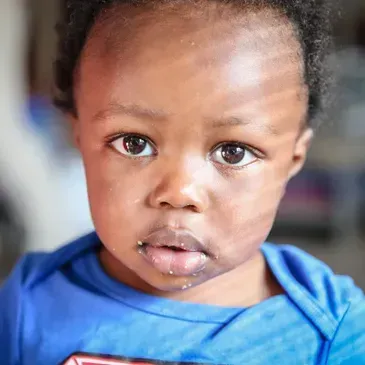 A close up of a baby wearing a blue shirt and looking at the camera.