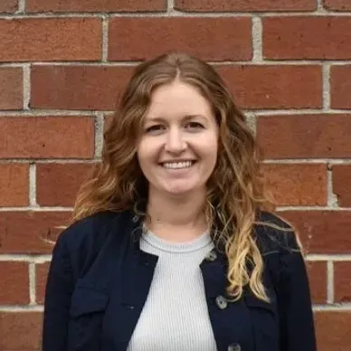 A woman is smiling in front of a brick wall.
