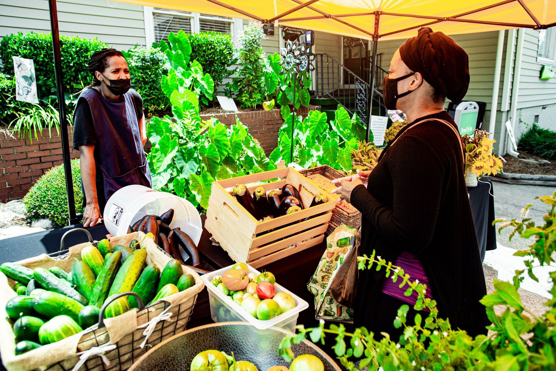 A woman wearing a mask is standing in front of a table full of fruits and vegetables.