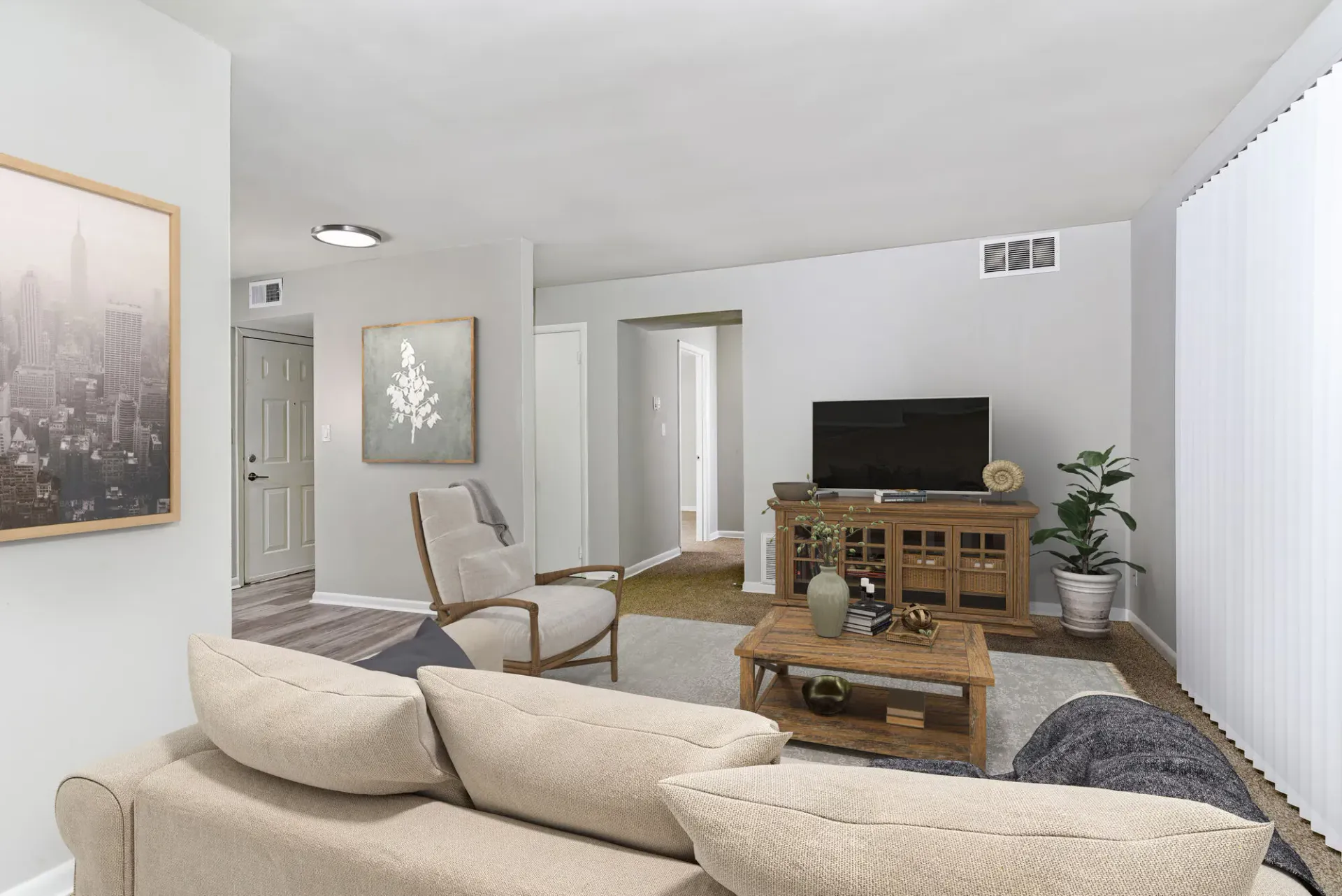 Living room in an apartment with beige sofa, coffee table, TV on a wooden console, plant. Contact our leasing team at Harborstone Apartments today to schedule a tour of our studio, one-, and two-bedroom apartments in Newport News, VA. 