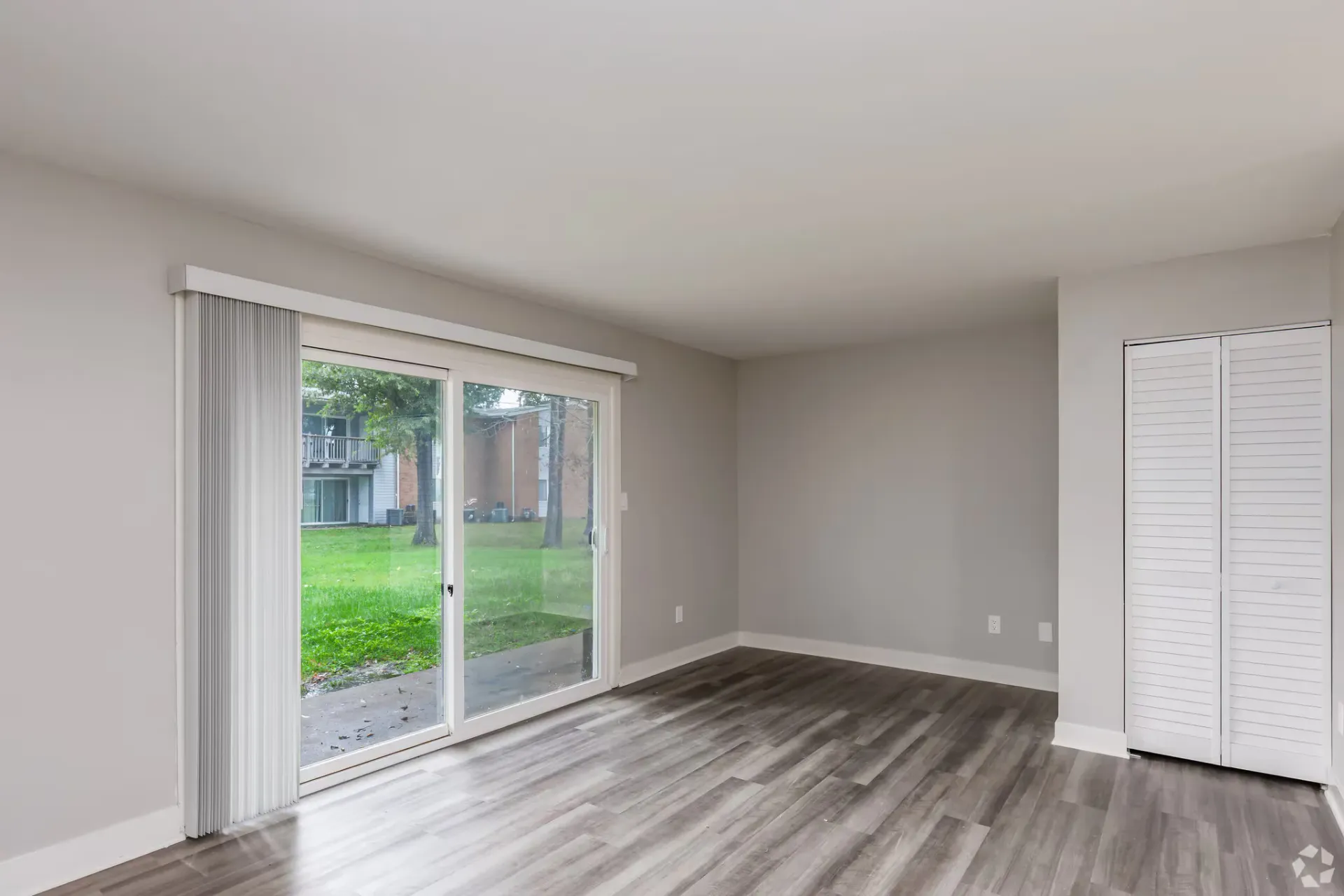 Empty apartment living room with sliding glass door to outdoors, vertical blinds, and a white closet. Contact our leasing team at Harborstone Apartments today to schedule a tour of our studio, one-, and two-bedroom apartments in Newport News, VA. 