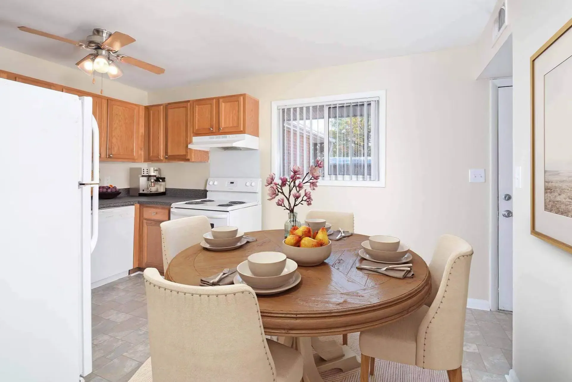 Apartment kitchen with wooden cabinets, white appliances, and a round dining table. Contact our leasing team at Harborstone Apartments today to schedule a tour of our studio, one-, and two-bedroom apartments in Newport News, VA. 