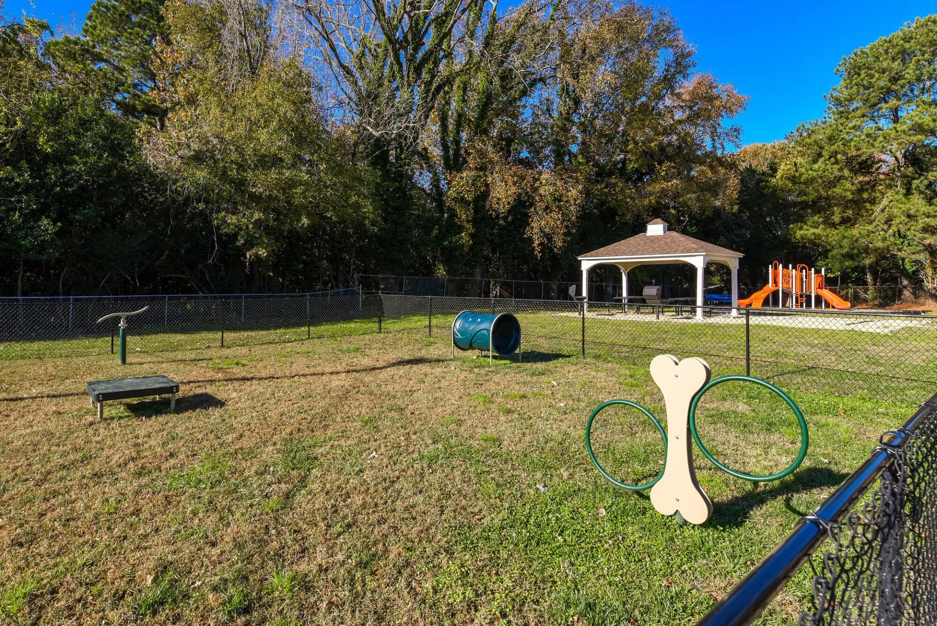 Fenced community playground with a pavilion, tunnel, round climbing structures, and an orange slide. Enjoy a variety of onsite community amenities at Harborstone Apartments in Newport News, VA. 