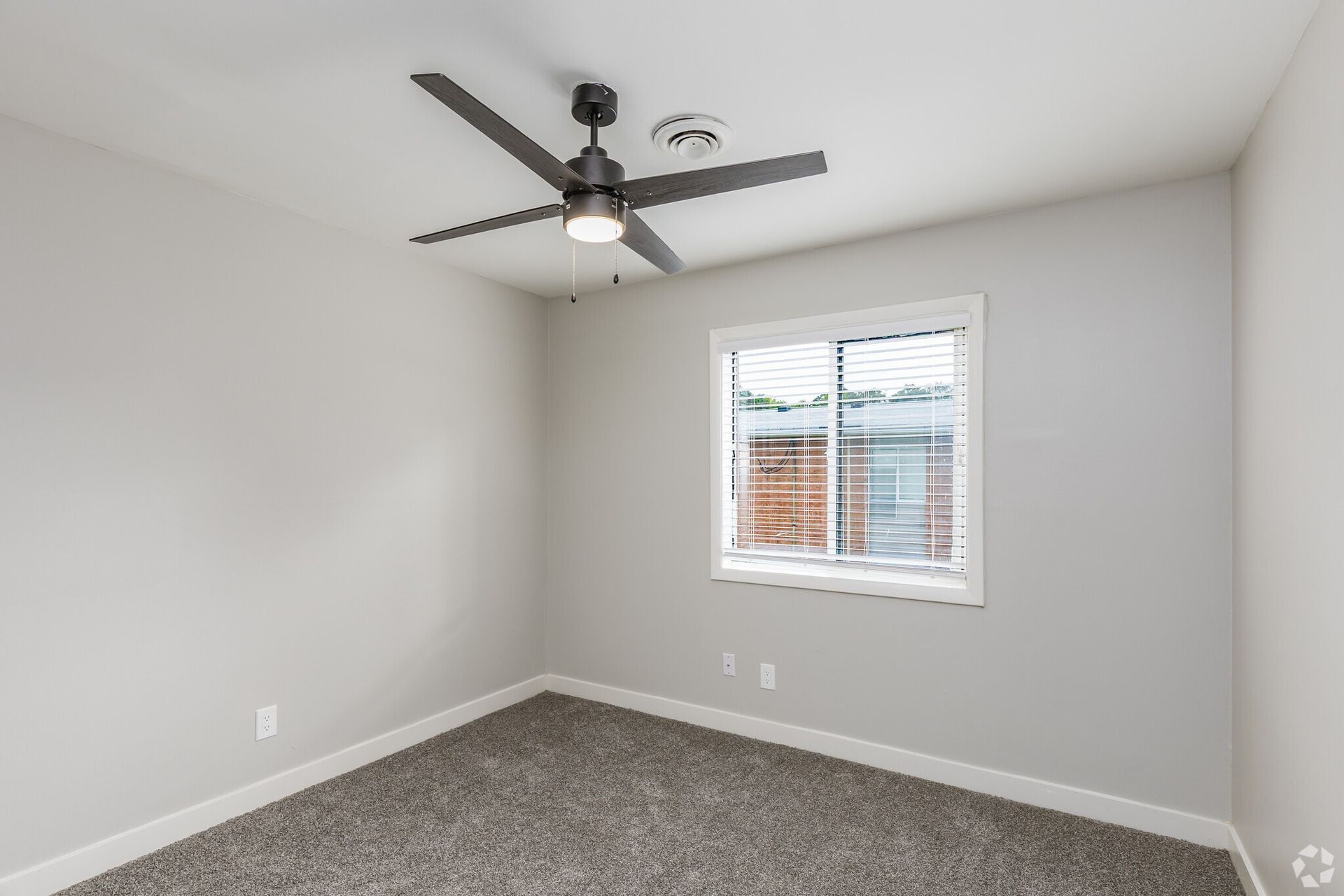 Empty bedroom with gray walls, carpet, a window with white blinds, and a ceiling fan. Contact our leasing team at Harborstone Apartments today to schedule a tour of our studio, one-, and two-bedroom apartments in Newport News, VA. 