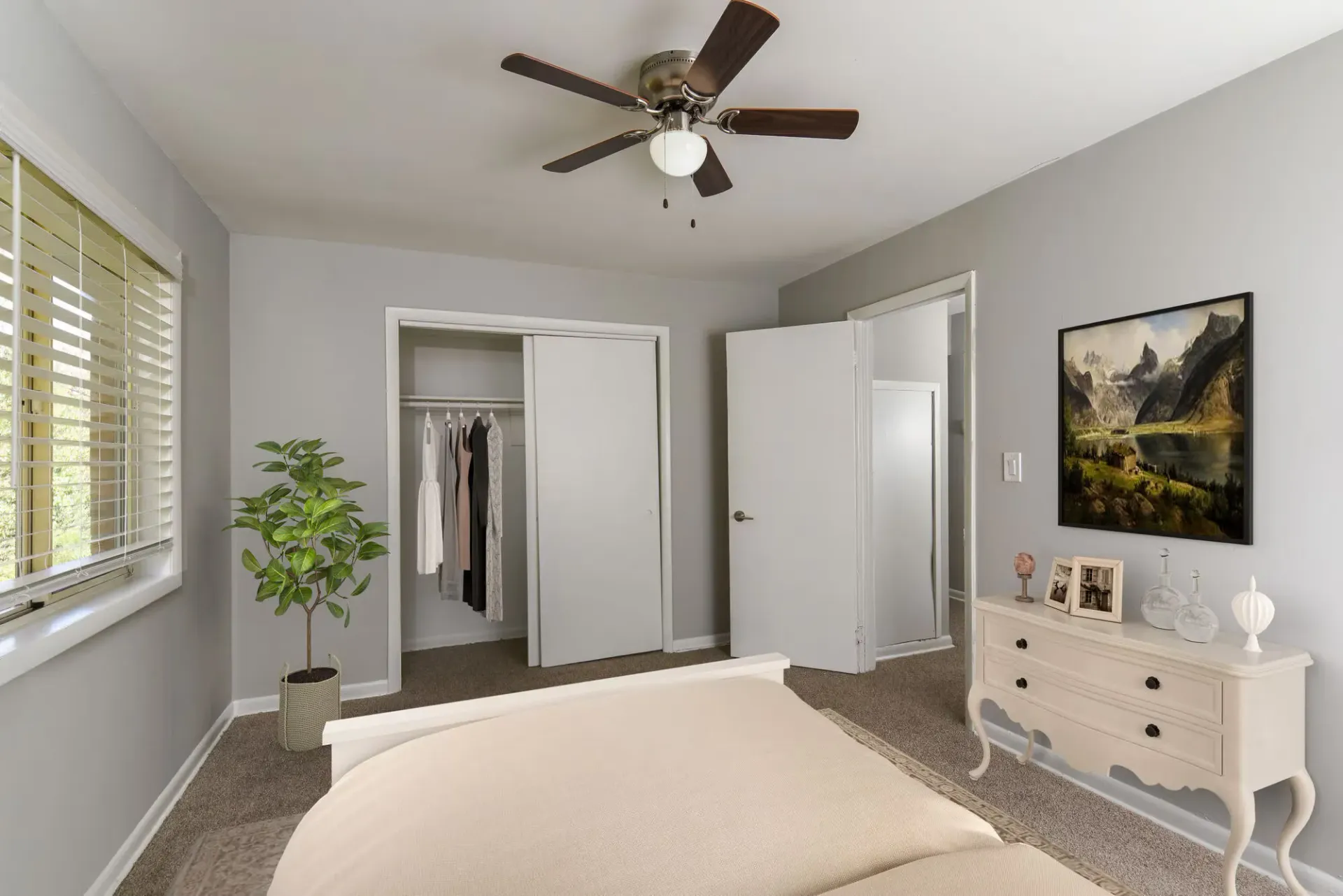 Bedroom interior with a bed, ceiling fan, window with blinds, dresser, and open closet with clothes. Contact our leasing team at Harborstone Apartments today to schedule a tour of our studio, one-, and two-bedroom apartments in Newport News, VA. 