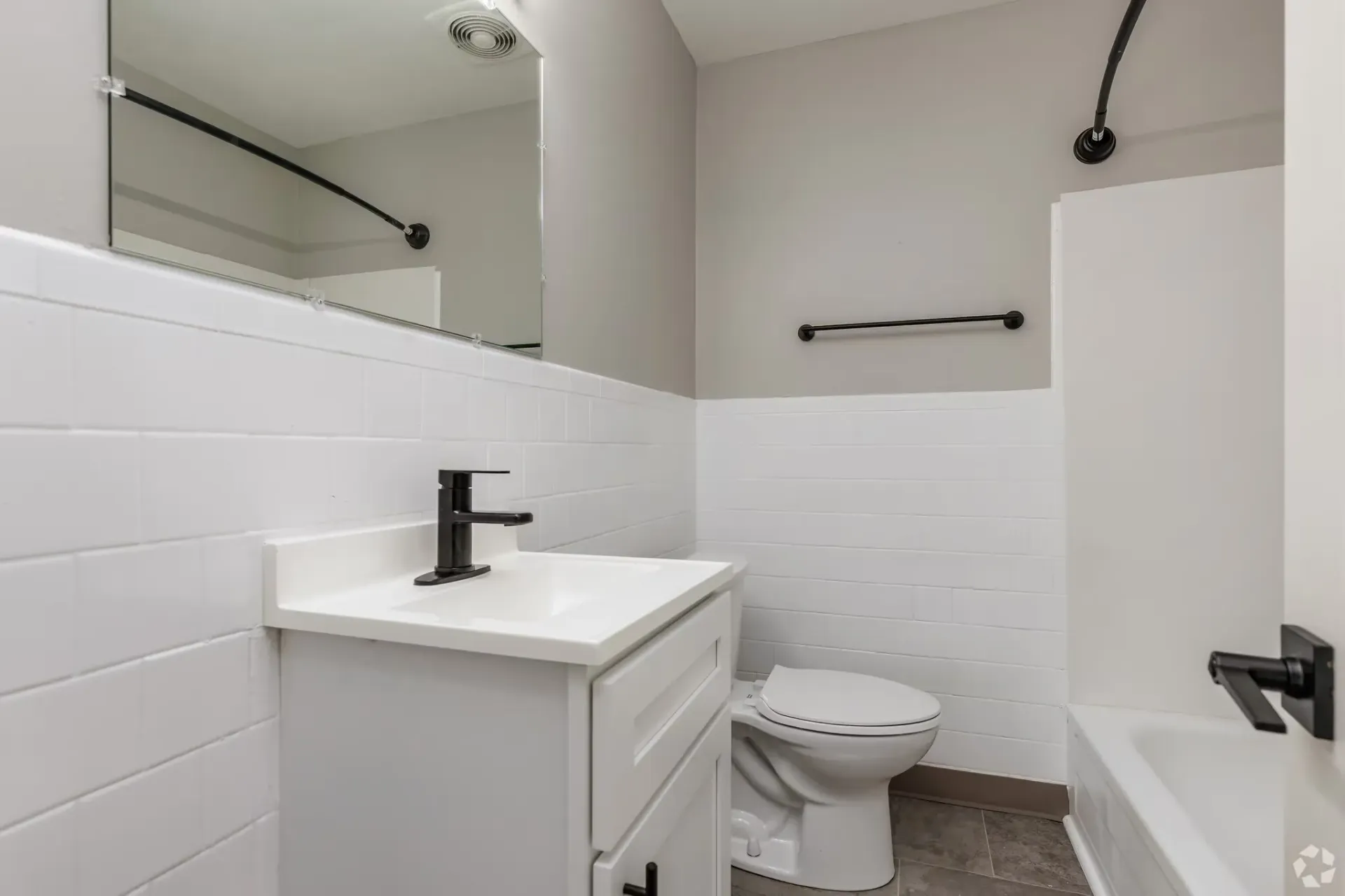 Modern apartment bathroom with white tile wainscoting, a white vanity, toilet, and a bathtub. Contact our leasing team at Harborstone Apartments today to schedule a tour of our studio, one-, and two-bedroom apartments in Newport News, VA. 