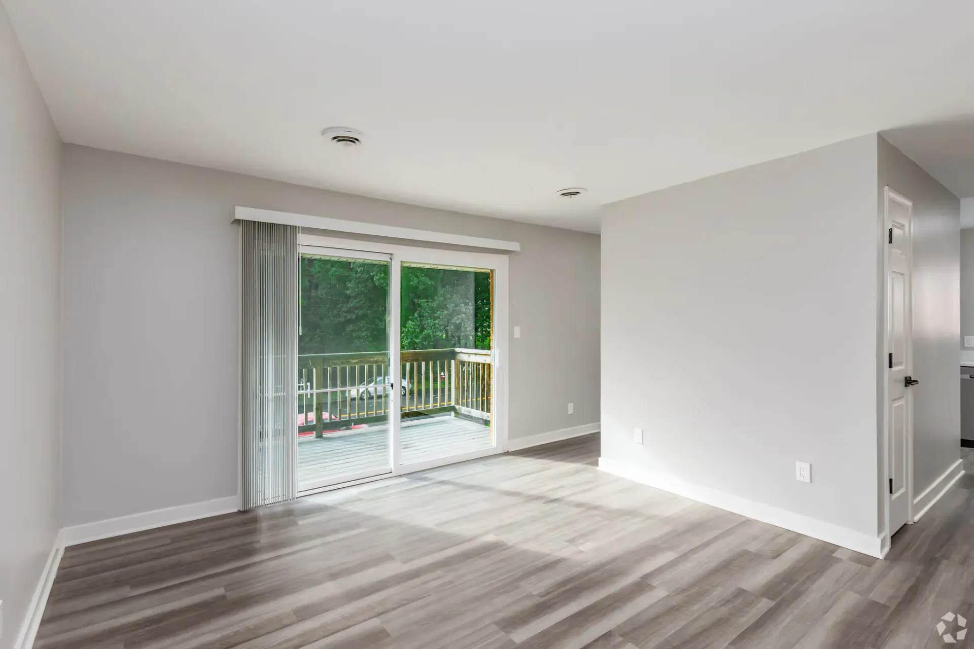 Bright living room with sliding glass doors to a balcony, light gray walls, and wood-look flooring. Contact our leasing team at Harborstone Apartments today to schedule a tour of our studio, one-, and two-bedroom apartments in Newport News, VA. 
