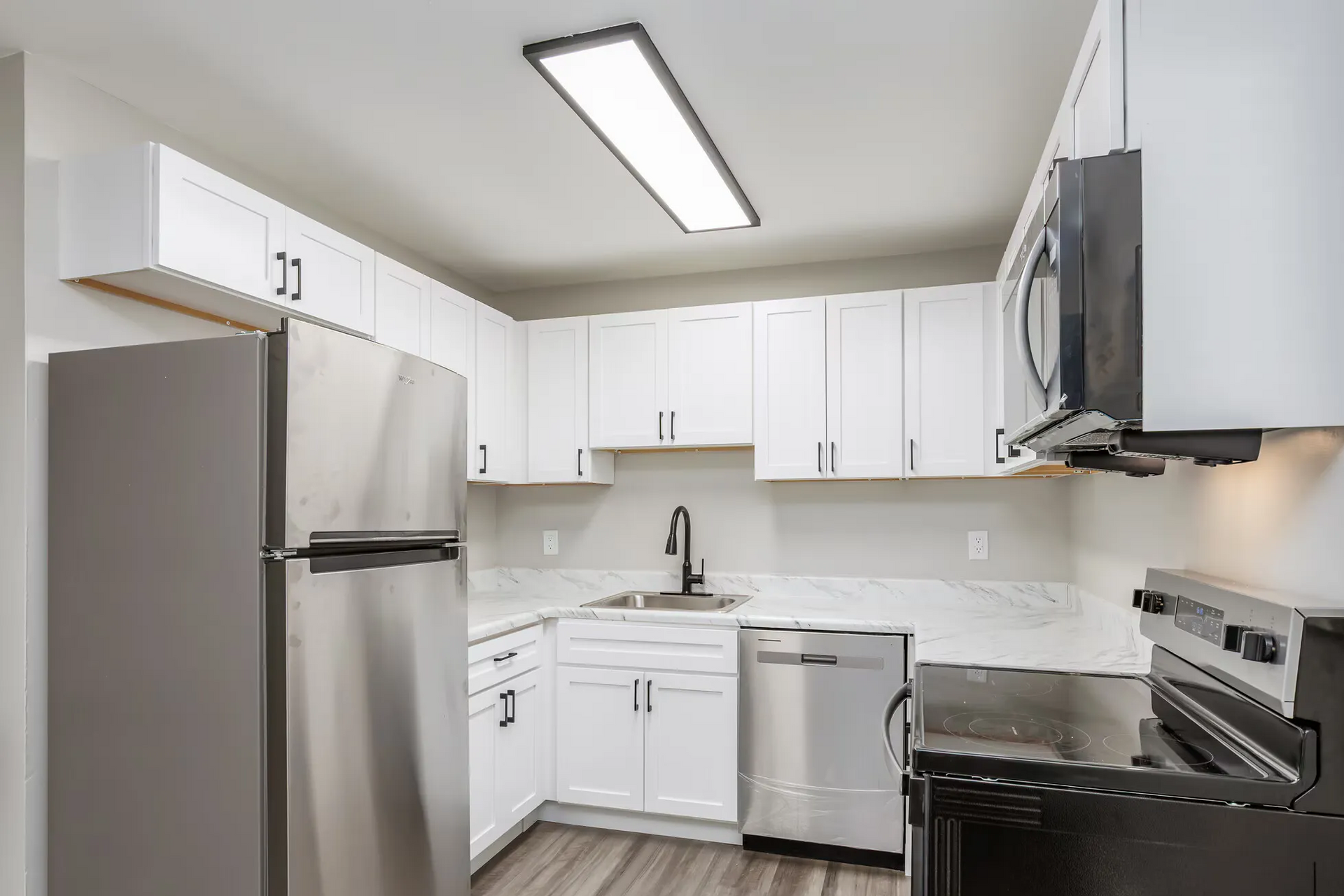 White kitchen with white cabinets, marble-look countertops, and stainless steel appliances. Contact our leasing team at Harborstone Apartments today to schedule a tour of our studio, one-, and two-bedroom apartments in Newport News, VA. 