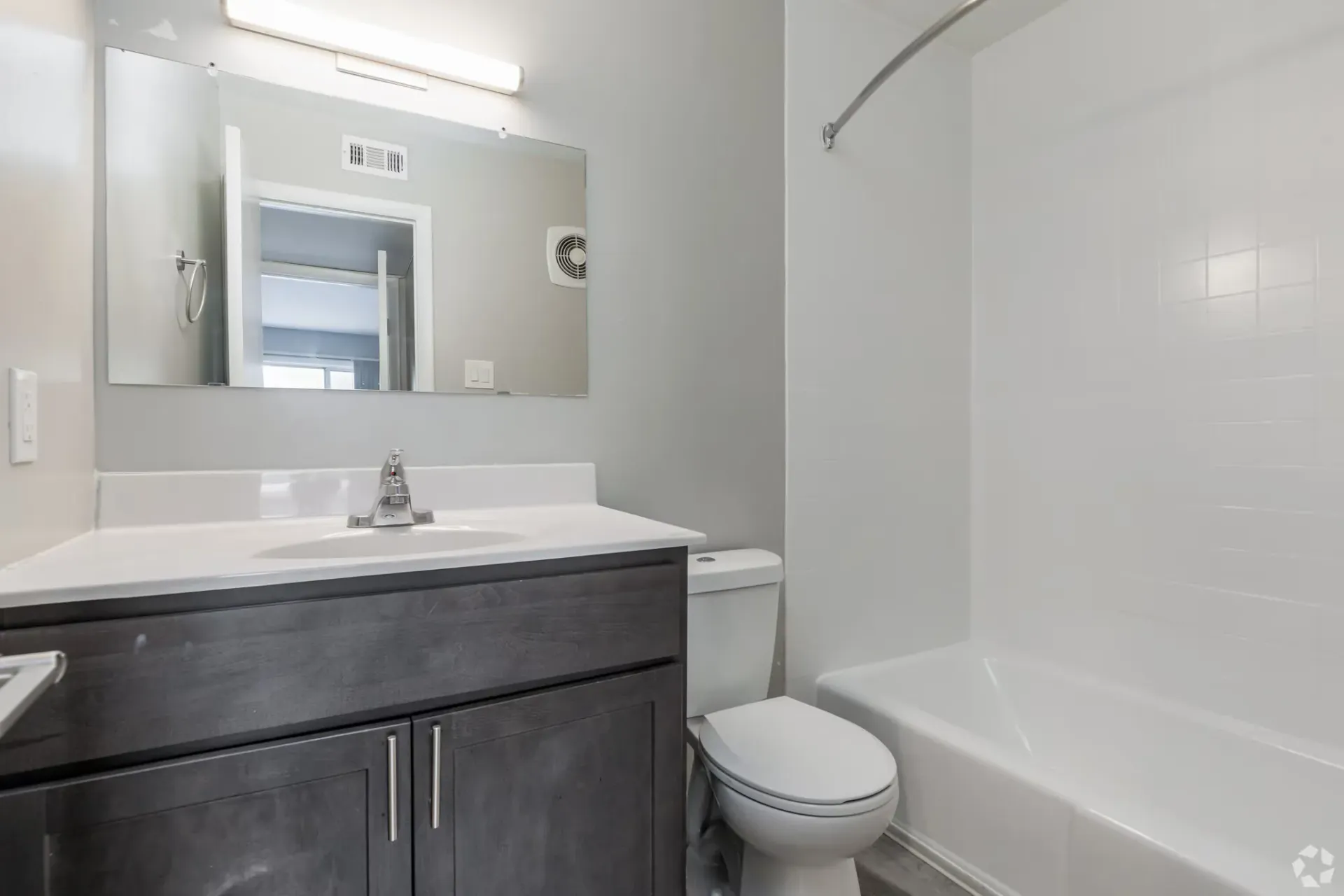 Bathroom with a dark wood vanity, mirror, toilet, and a white bathtub/shower combo. Contact our leasing team at Harborstone Apartments today to schedule a tour of our studio, one-, and two-bedroom apartments in Newport News, VA. 