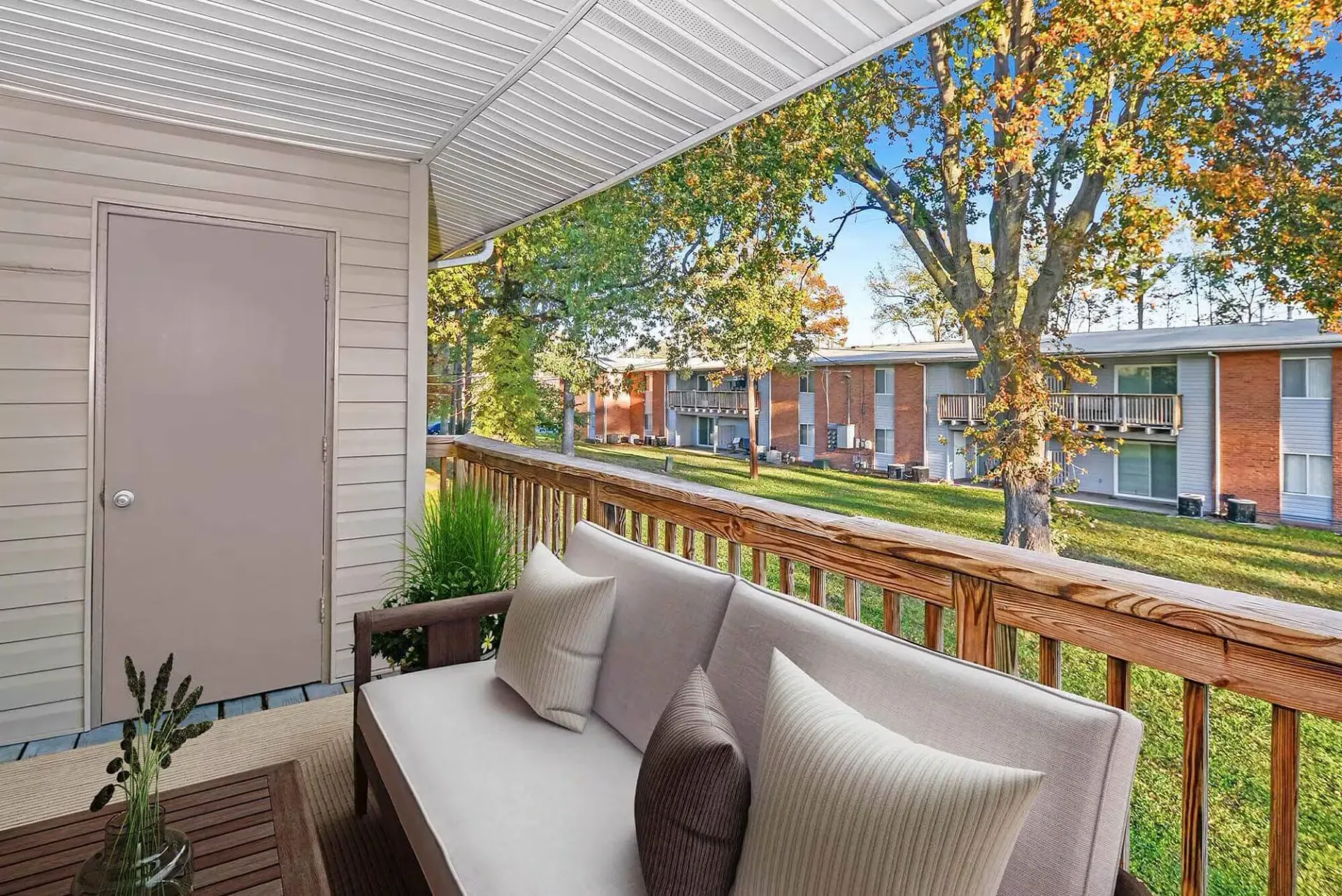 Covered balcony with cushioned outdoor sofa and pillows, overlooking a green lawn and neighboring apartment buildings. Contact our leasing team at Harborstone Apartments today to schedule a tour of our studio, one-, and two-bedroom apartments in Newport News, VA. 