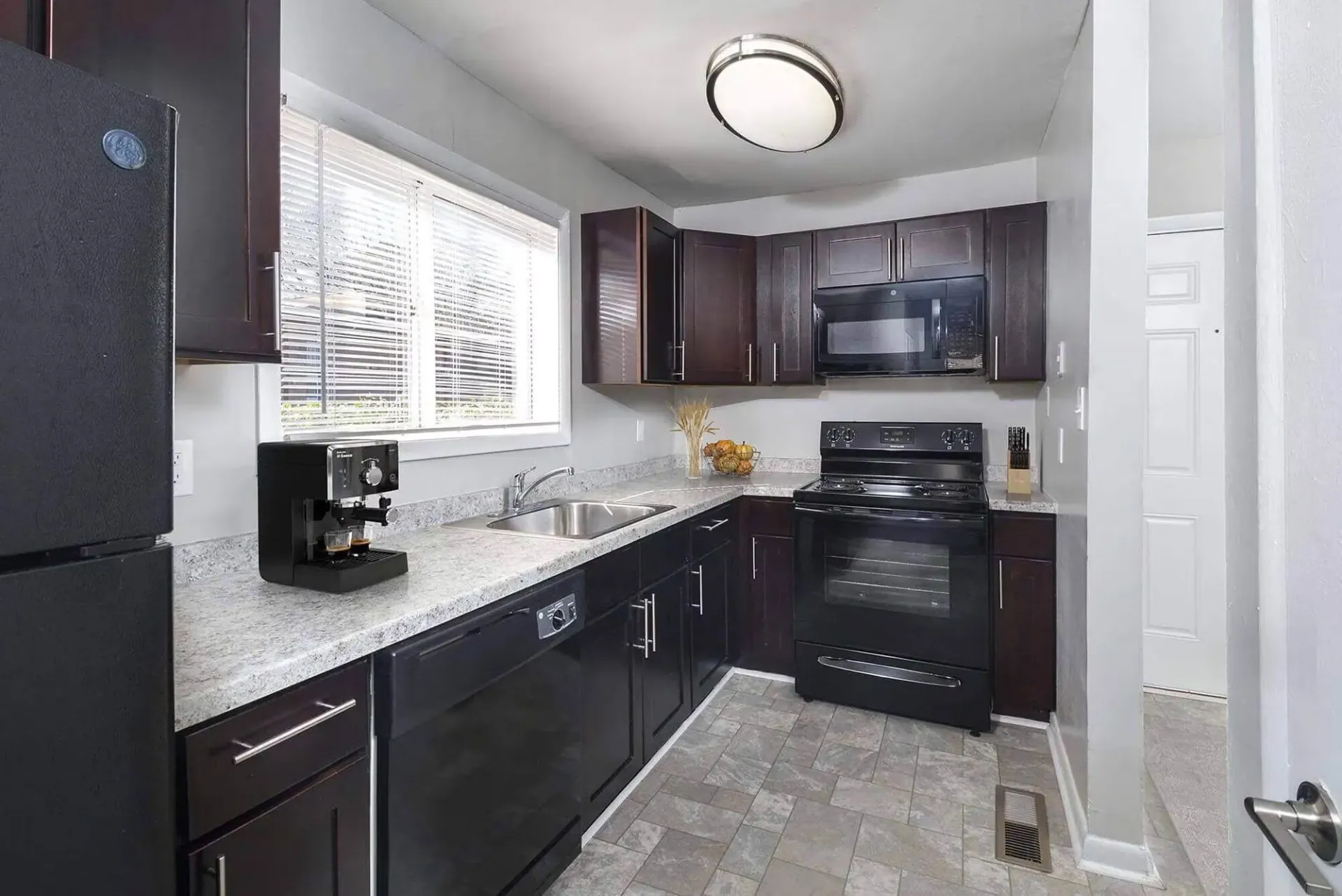 Kitchen in an apartment unit with dark wood cabinets, black appliances, and granite countertops. Contact our leasing team at Harborstone Apartments today to schedule a tour of our studio, one-, and two-bedroom apartments in Newport News, VA. 