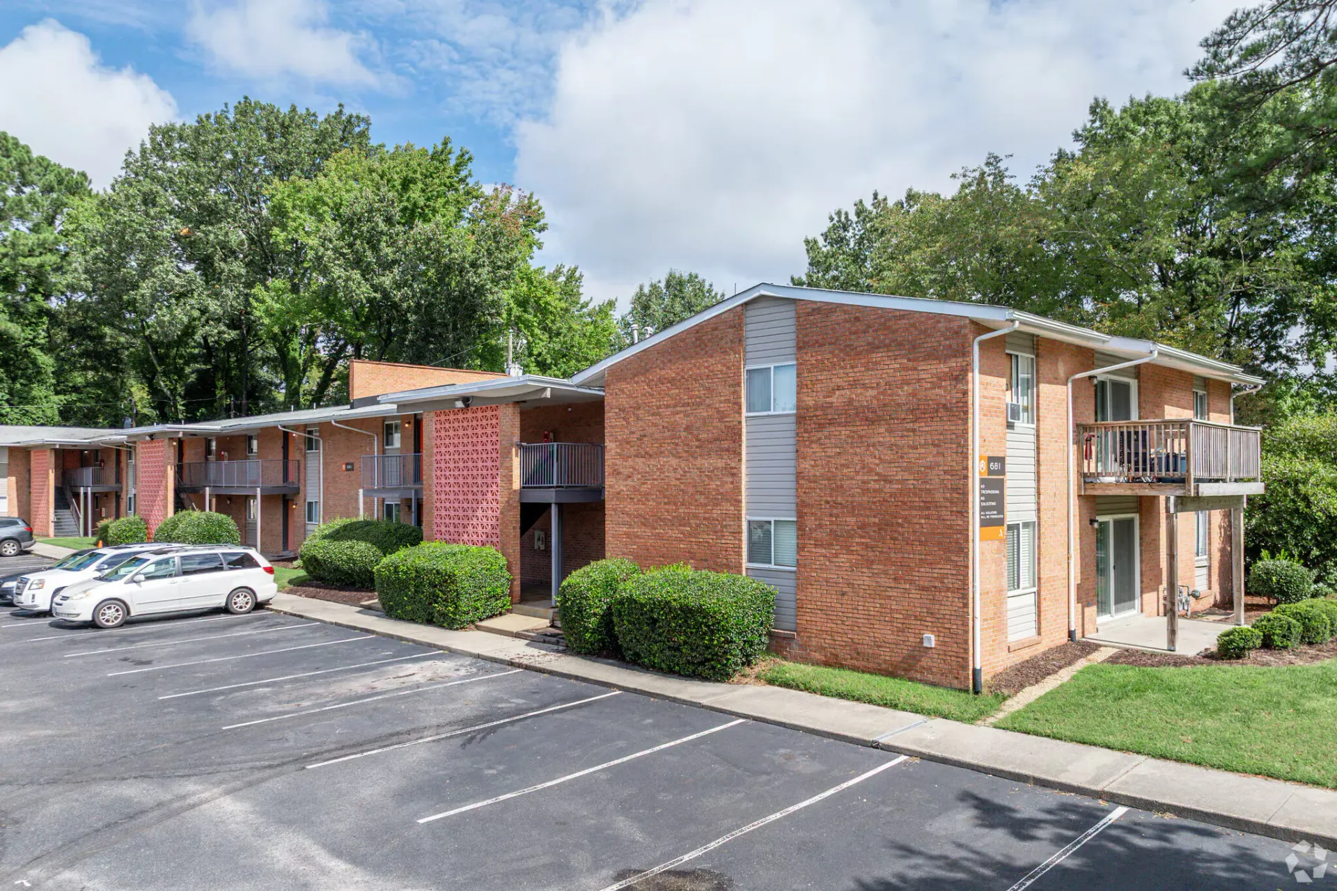 Exterior view of a brick apartment building with a parking lot and trees. Welcome home to Harborstone Apartments, offering studio, 1, and 2-bedroom apartments for rent in New Port News, VA.