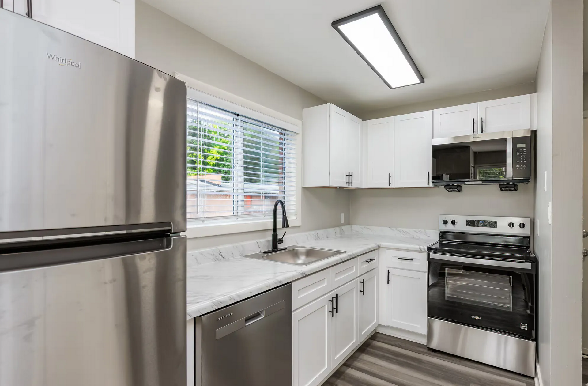 Modern white kitchen with stainless steel fridge, stove, and sink. Contact our leasing team at Harborstone Apartments today to schedule a tour of our studio, one-, and two-bedroom apartments in Newport News, VA. 