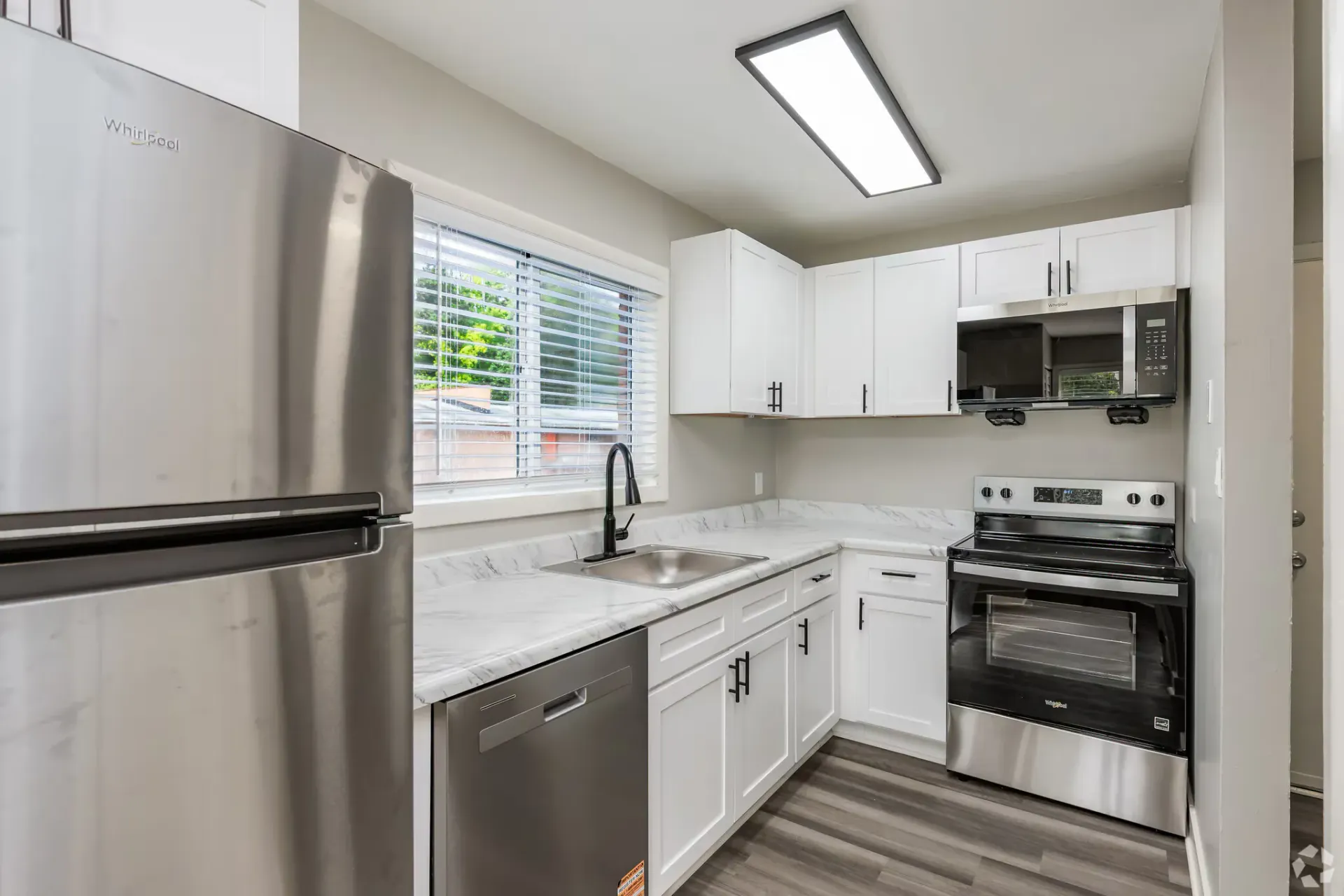 Modern white kitchen with stainless steel fridge, stove, and sink. Contact our leasing team at Harborstone Apartments today to schedule a tour of our studio, one-, and two-bedroom apartments in Newport News, VA. 