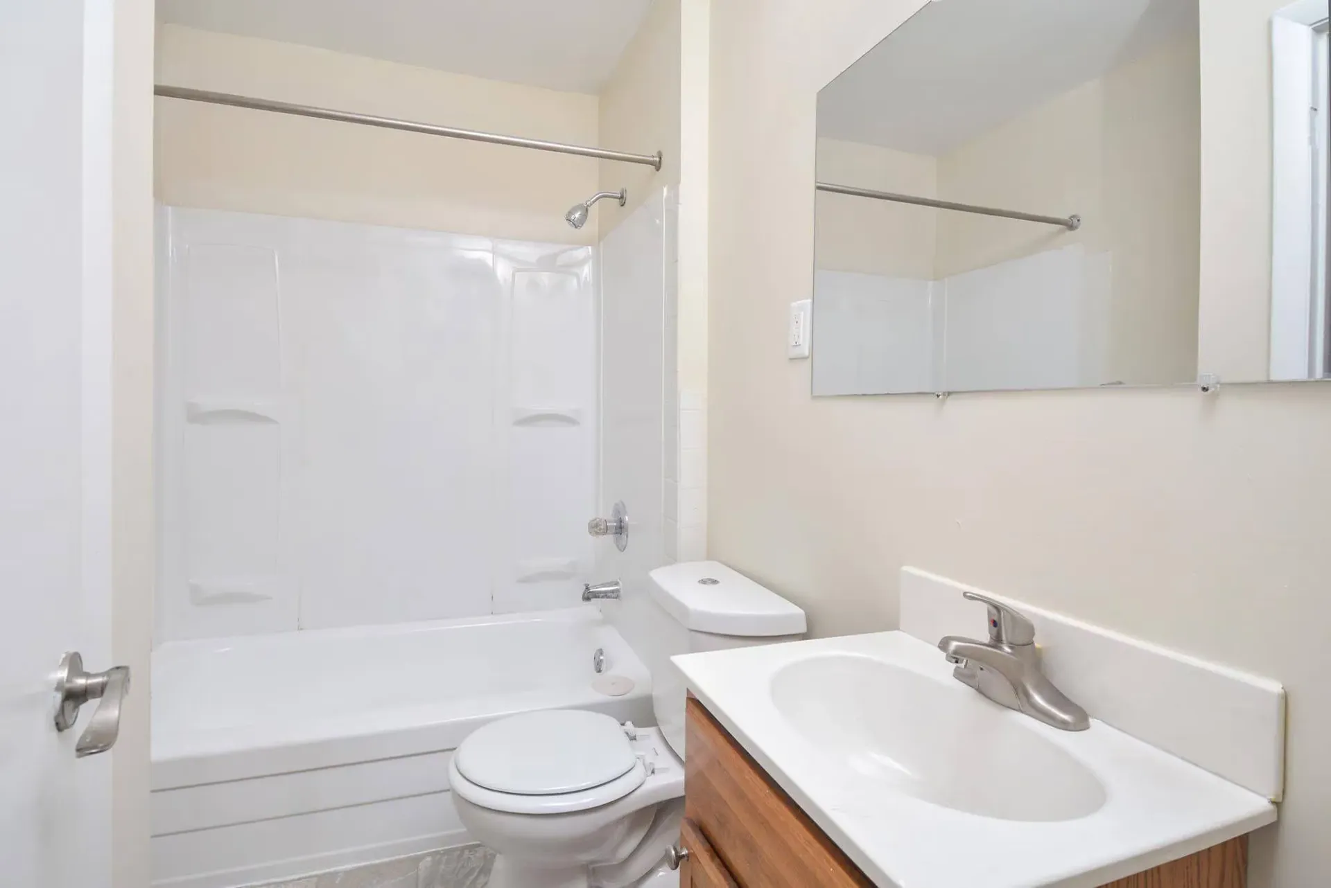 Bathroom with white tub/shower, toilet, and sink with a mirror. Contact our leasing team at Harborstone Apartments today to schedule a tour of our studio, one-, and two-bedroom apartments in Newport News, VA. 