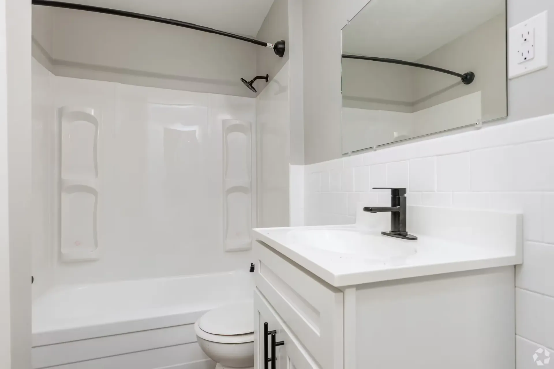 White bathroom with tub/shower, vanity, and large mirror. Contact our leasing team at Harborstone Apartments today to schedule a tour of our studio, one-, and two-bedroom apartments in Newport News, VA. 