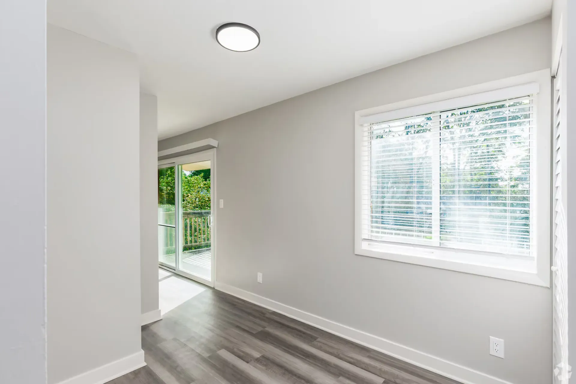 Interior of an apartment with a window and sliding glass door to a balcony, gray walls, and dark flooring. Contact our leasing team at Harborstone Apartments today to schedule a tour of our studio, one-, and two-bedroom apartments in Newport News, VA. 