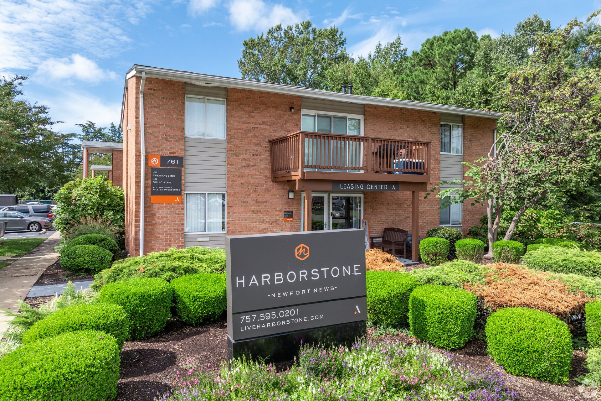 Exterior view of a brick-architecture apartment community with parking, landscaping, and balconies.