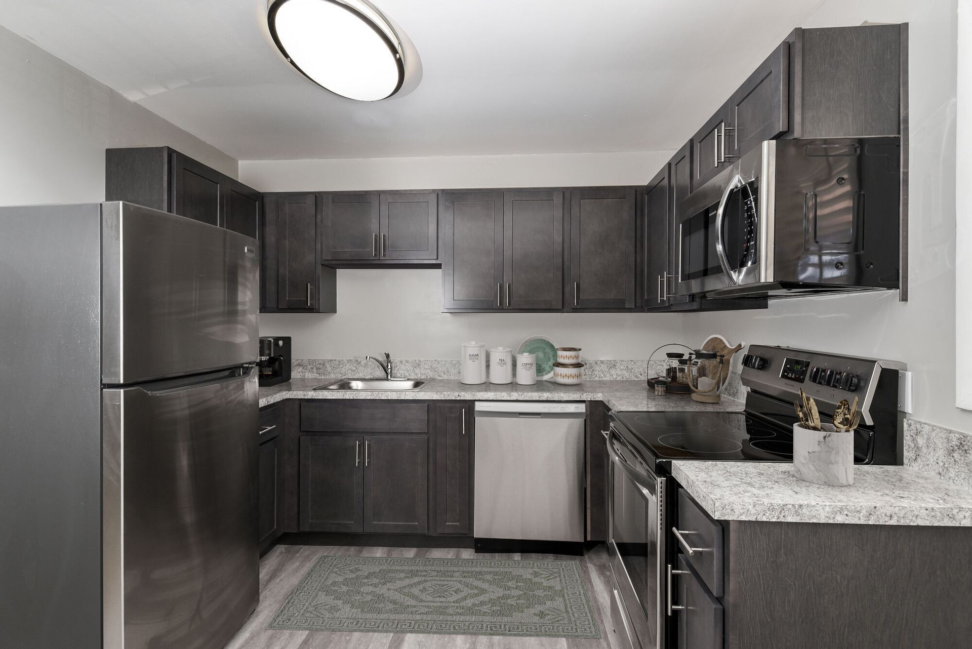 Modern dark-wood kitchen with stainless steel fridge, dishwasher, microwave, and stove. Contact our leasing team at Harborstone Apartments today to schedule a tour of our studio, one-, and two-bedroom apartments in Newport News, VA. 