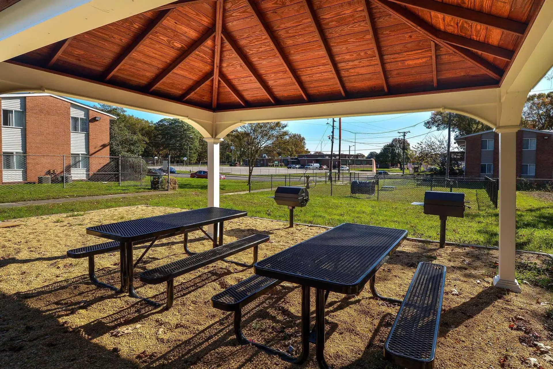 Covered outdoor pavilion with metal picnic tables and grills in a grassy apartment complex courtyard. Enjoy a variety of onsite community amenities at Harborstone Apartments in Newport News, VA. 
