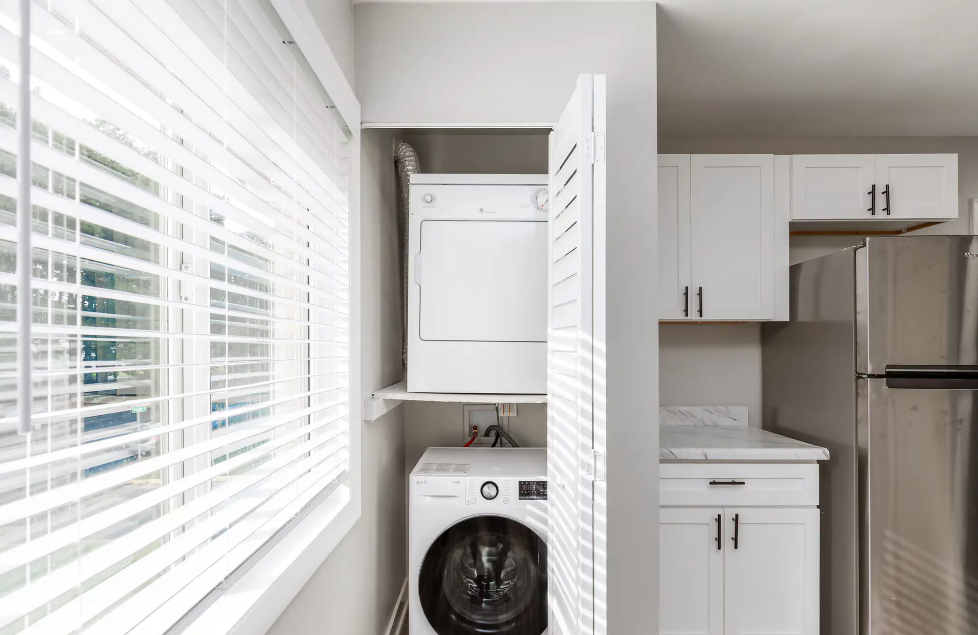 Stacked washer and dryer in a compact laundry closet beside white kitchen cabinets. Contact our leasing team at Harborstone Apartments today to schedule a tour of our studio, one-, and two-bedroom apartments in Newport News, VA. 