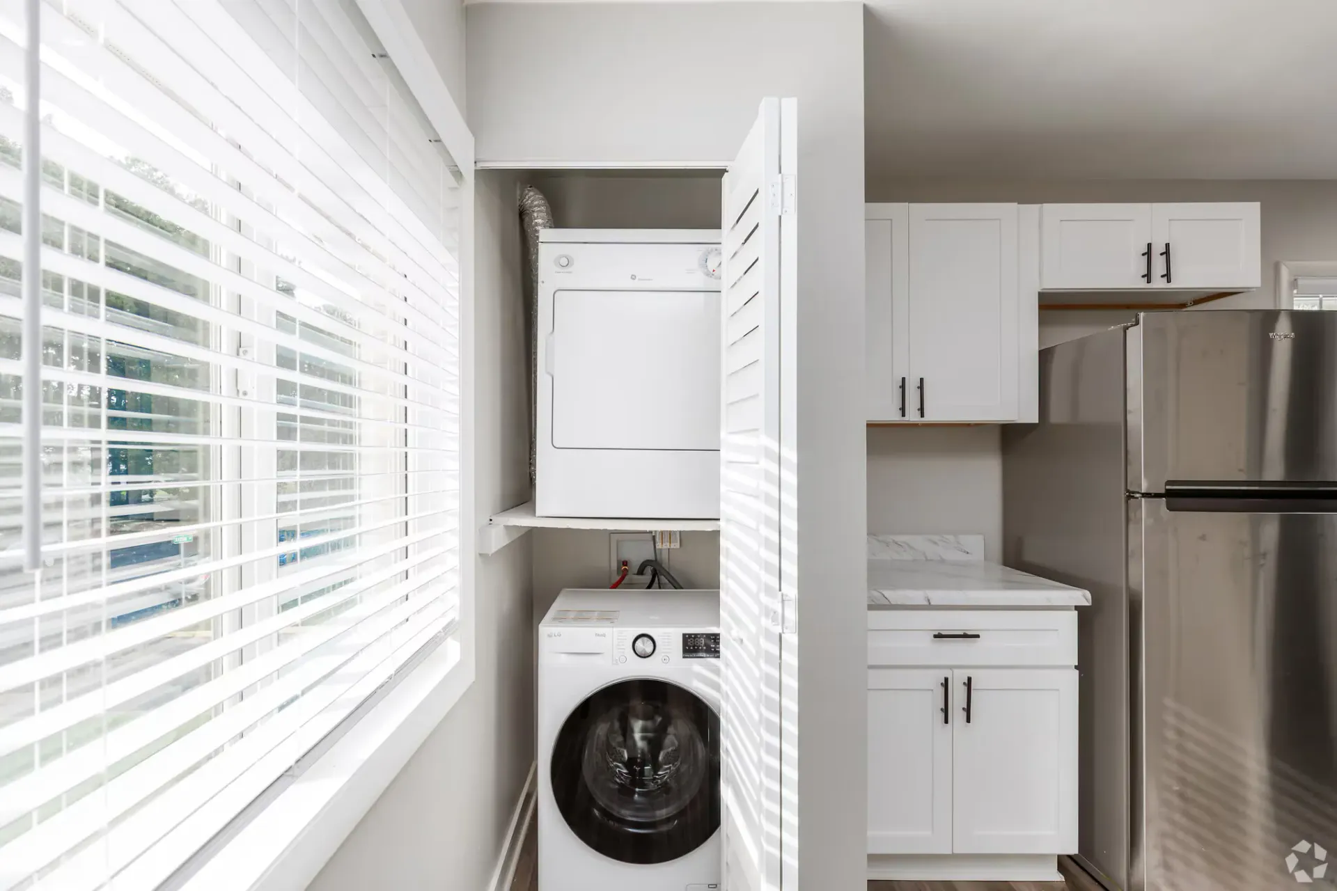 Stacked washer and dryer in a compact laundry closet beside white kitchen cabinets. Contact our leasing team at Harborstone Apartments today to schedule a tour of our studio, one-, and two-bedroom apartments in Newport News, VA. 