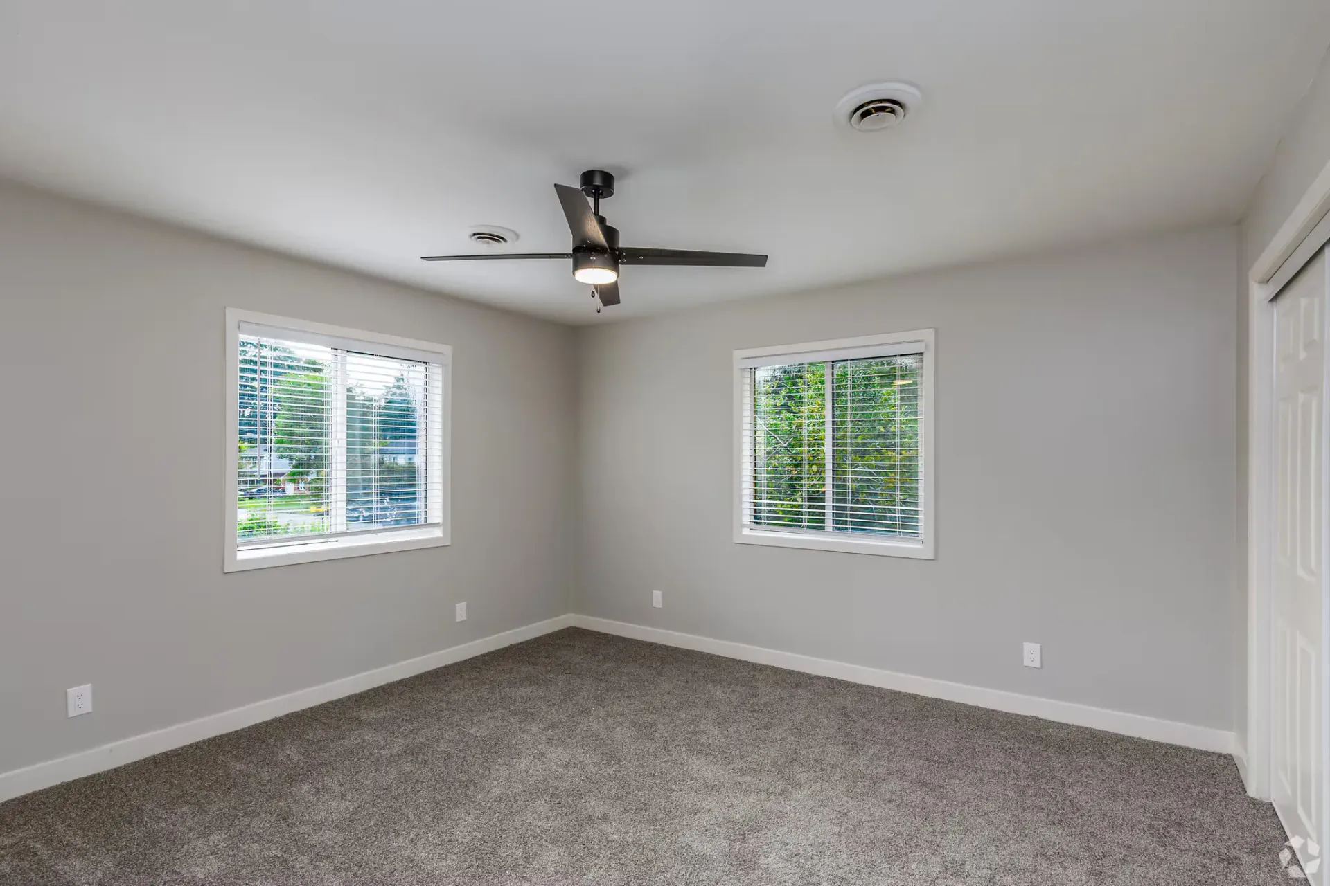 Bedroom in an apartment with two windows, blinds, ceiling fan, and beige walls. Contact our leasing team at Harborstone Apartments today to schedule a tour of our studio, one-, and two-bedroom apartments in Newport News, VA. 