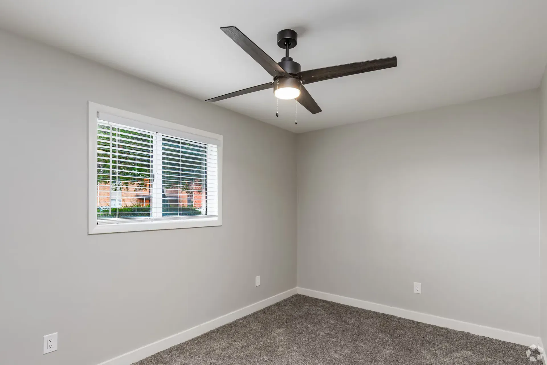Vacant bedroom with neutral gray walls, a window with blinds, and a dark ceiling fan. Contact our leasing team at Harborstone Apartments today to schedule a tour of our studio, one-, and two-bedroom apartments in Newport News, VA. 