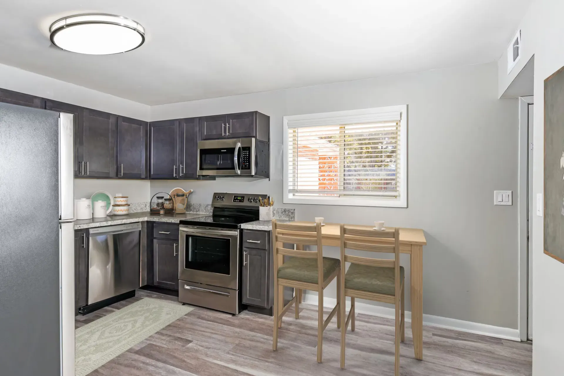 Kitchen in a modern apartment with dark cabinetry, stainless appliances, and a small dining table. Contact our leasing team at Harborstone Apartments today to schedule a tour of our studio, one-, and two-bedroom apartments in Newport News, VA. 