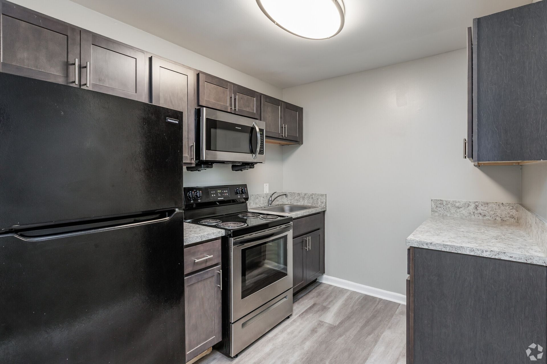 Modern apartment kitchen with black appliances, dark cabinets, and light countertops. Contact our leasing team at Harborstone Apartments today to schedule a tour of our studio, one-, and two-bedroom apartments in Newport News, VA. 