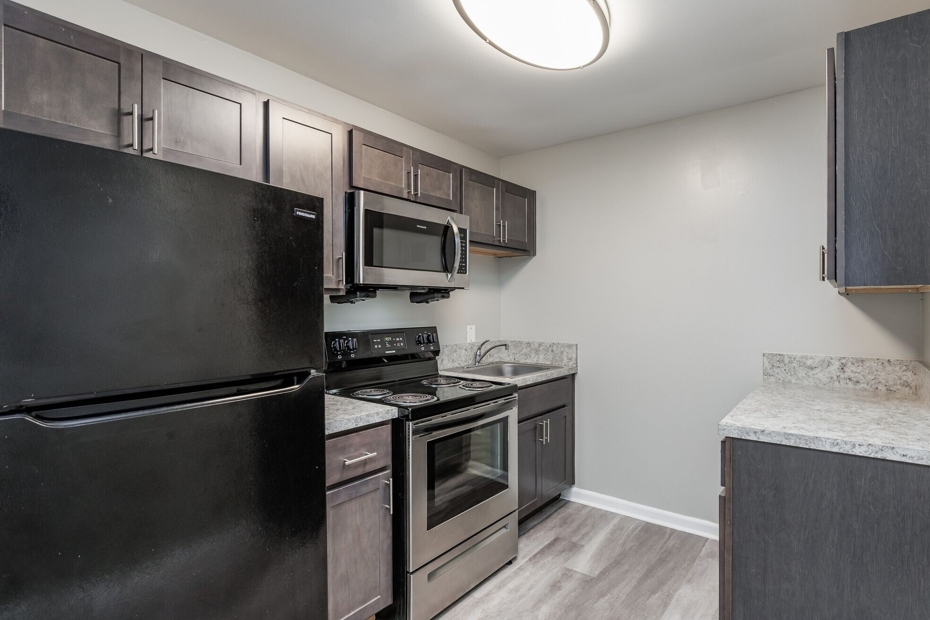 Modern apartment kitchen with black appliances, dark cabinets, and light countertops. Contact our leasing team at Harborstone Apartments today to schedule a tour of our studio, one-, and two-bedroom apartments in Newport News, VA. 