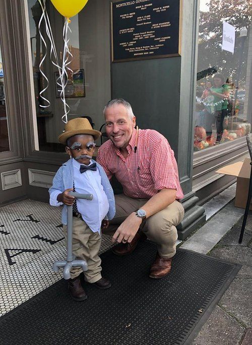 A man is kneeling next to a little boy dressed as an old man.