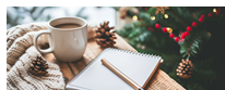 A cup of coffee , a notebook and a pen are on a table in front of a christmas tree.