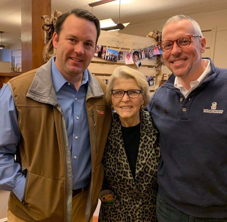 Two men and a woman posing for a picture with a man wearing a sweater with a lion on it