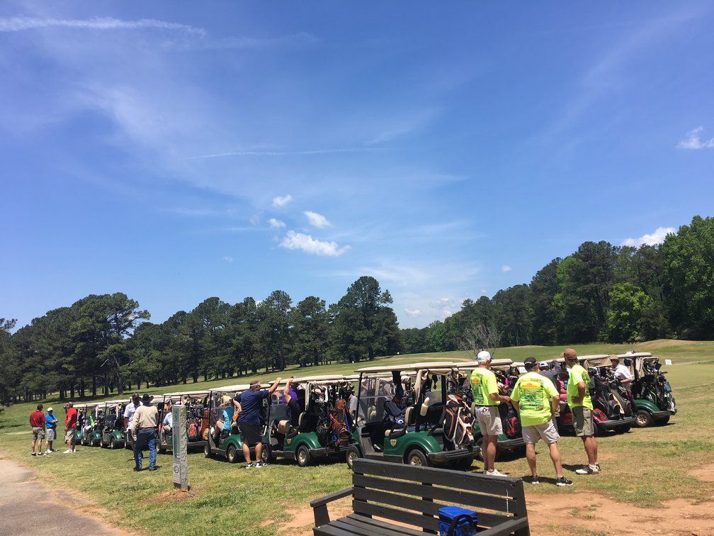 A group of people are standing in front of a row of golf carts on a golf course.