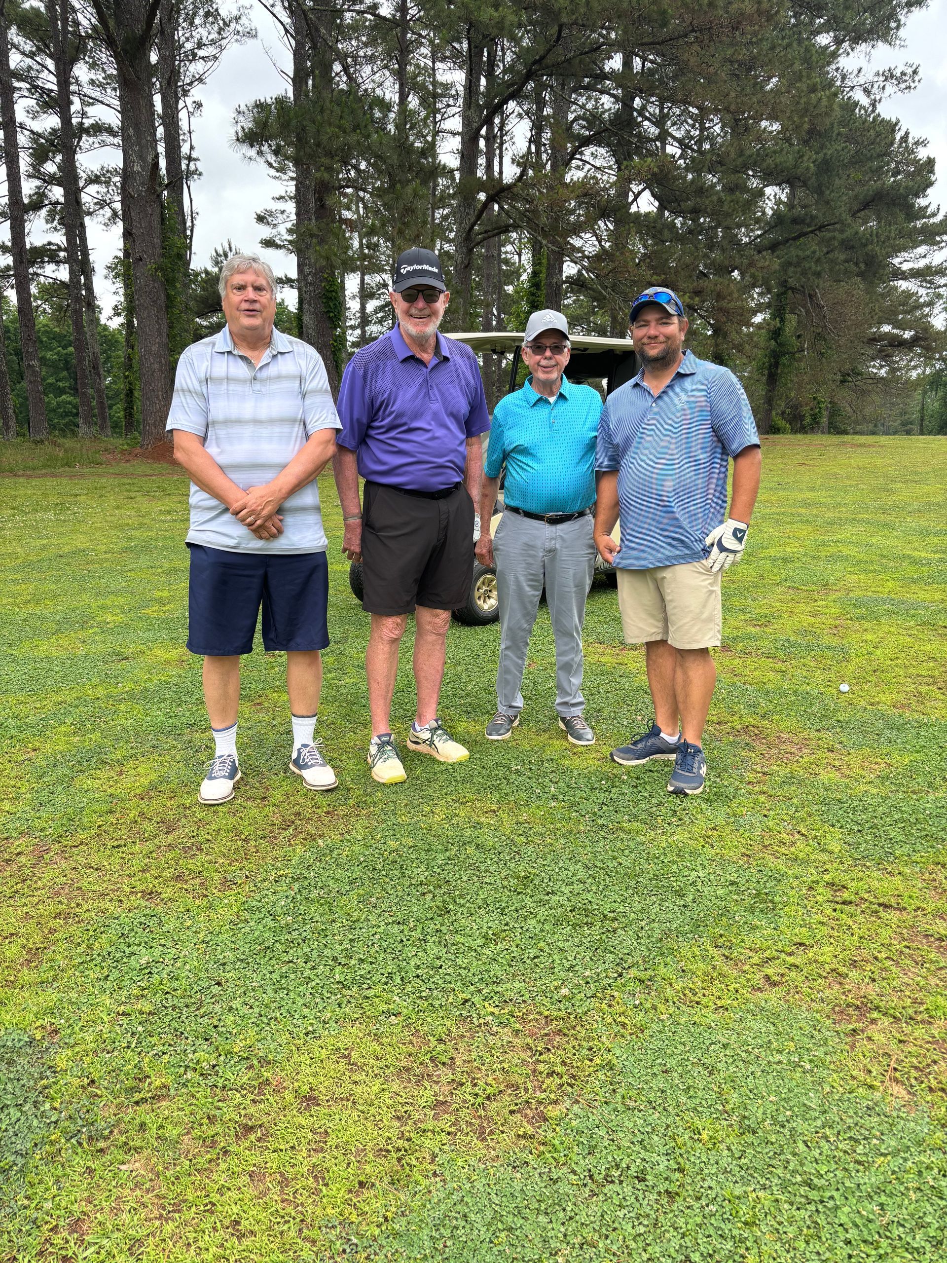 A group of people are standing in front of a row of golf carts on a golf course.