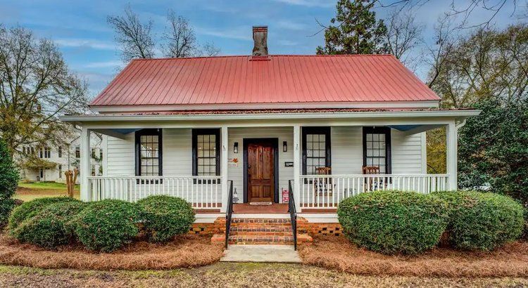 A small white house with a red roof and a porch.